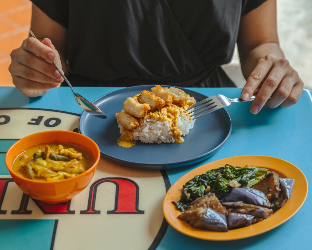 Person seated at a table with three dishes of food in front of them, including cultivated chicken and curry rice