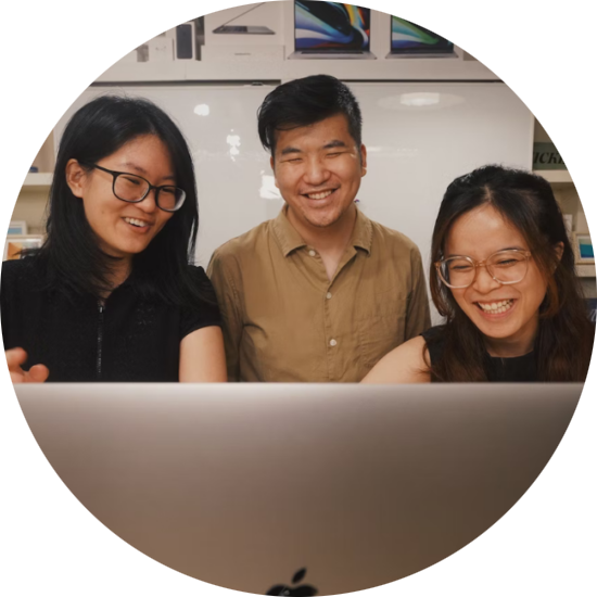 Three Asian persons looking at a computer and smiling